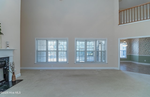 unfurnished living room featuring carpet, a premium fireplace, and a towering ceiling