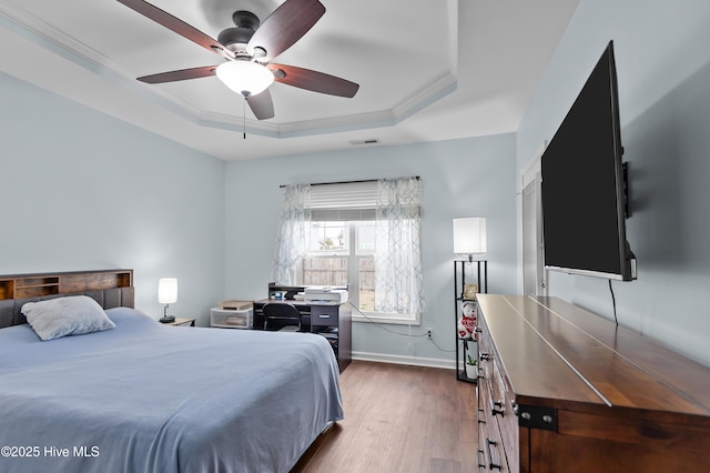 bedroom with crown molding, dark hardwood / wood-style floors, a raised ceiling, and ceiling fan