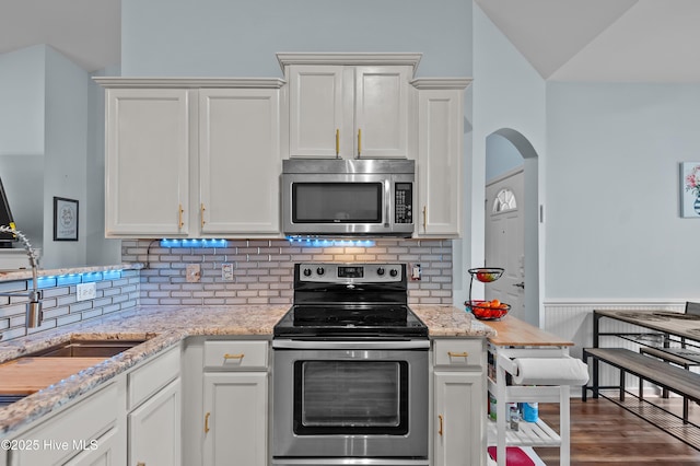 kitchen with stainless steel appliances, white cabinetry, and light stone countertops