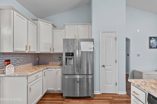 kitchen with lofted ceiling, stainless steel fridge, light hardwood / wood-style flooring, light stone countertops, and white cabinets