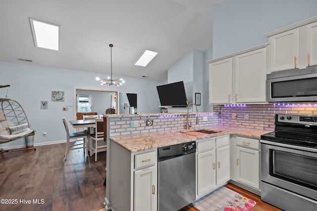 kitchen with sink, white cabinetry, light stone counters, appliances with stainless steel finishes, and kitchen peninsula