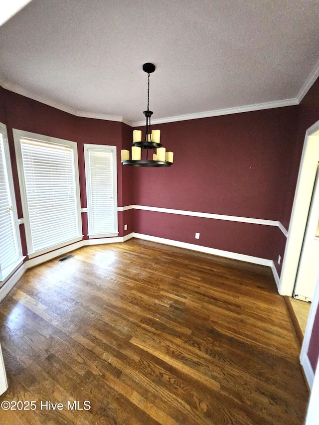 unfurnished dining area featuring dark hardwood / wood-style flooring, ornamental molding, and an inviting chandelier