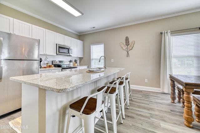 kitchen with a breakfast bar, light stone counters, appliances with stainless steel finishes, a kitchen island with sink, and white cabinets