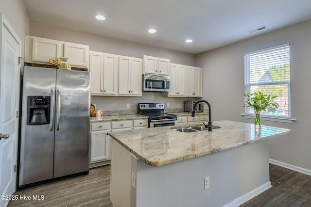 kitchen with light stone countertops, sink, stainless steel appliances, a center island with sink, and white cabinets