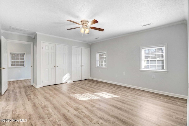 unfurnished bedroom with multiple windows, a textured ceiling, multiple closets, and light wood-type flooring