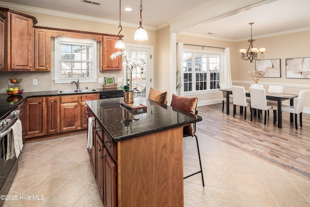 kitchen with sink, decorative light fixtures, ornamental molding, a notable chandelier, and a kitchen island