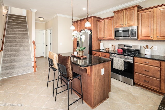 kitchen with light tile patterned floors, dark stone counters, pendant lighting, a kitchen island, and appliances with stainless steel finishes