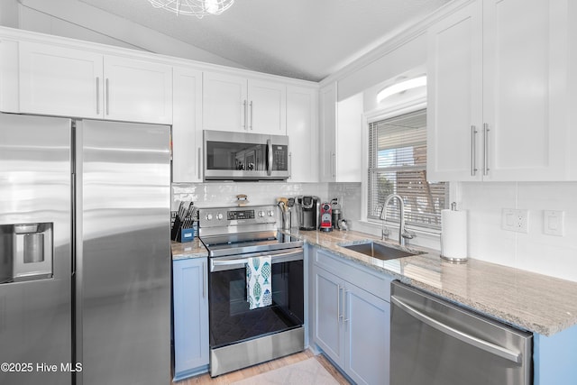 kitchen with white cabinetry, sink, light stone countertops, lofted ceiling, and appliances with stainless steel finishes