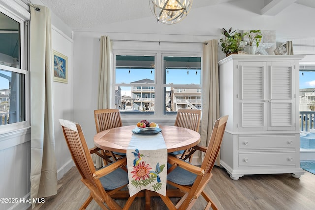 dining room featuring hardwood / wood-style flooring, a chandelier, a textured ceiling, and vaulted ceiling