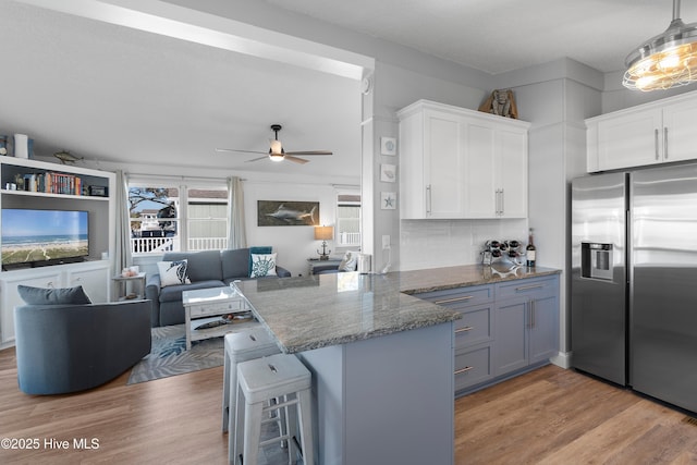 kitchen featuring kitchen peninsula, stainless steel refrigerator with ice dispenser, white cabinets, and a kitchen breakfast bar