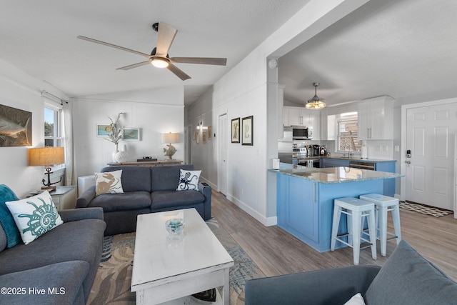 living room with light wood-type flooring, ceiling fan, lofted ceiling, and sink