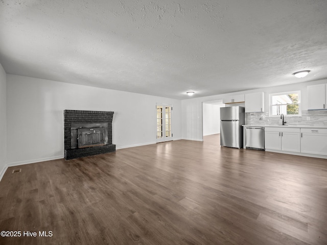 unfurnished living room featuring sink, a brick fireplace, a textured ceiling, and dark hardwood / wood-style floors