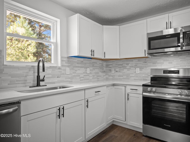 kitchen with appliances with stainless steel finishes, dark wood-type flooring, sink, white cabinetry, and tasteful backsplash