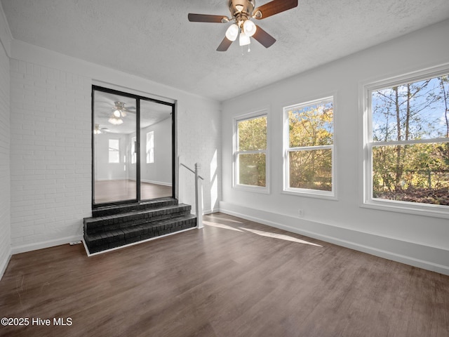 unfurnished living room featuring brick wall, a textured ceiling, and dark hardwood / wood-style floors