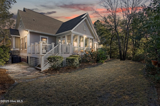 back house at dusk featuring cooling unit, a lawn, and a sunroom