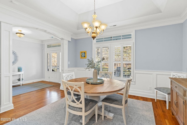 dining space featuring decorative columns, wood-type flooring, an inviting chandelier, and crown molding