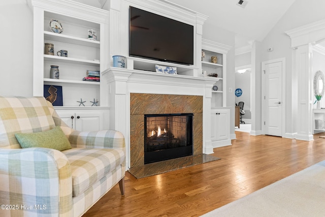 living room with lofted ceiling, a fireplace, built in features, and light wood-type flooring