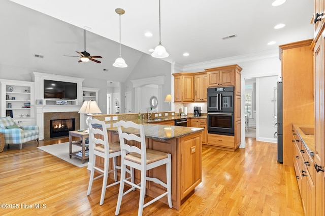 kitchen featuring kitchen peninsula, a kitchen breakfast bar, dark stone counters, black appliances, and light wood-type flooring