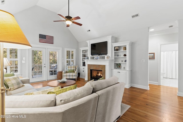 living room featuring high vaulted ceiling, a fireplace, hardwood / wood-style flooring, ceiling fan, and french doors