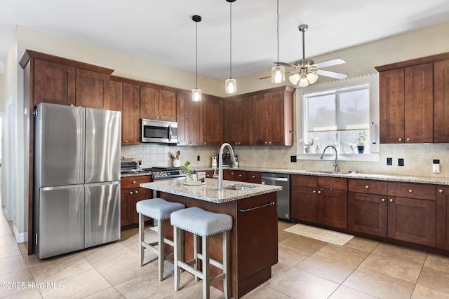 kitchen featuring a center island with sink, stainless steel appliances, a kitchen breakfast bar, light stone counters, and sink