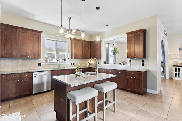 kitchen with dishwasher, sink, a kitchen island with sink, a kitchen breakfast bar, and light stone counters