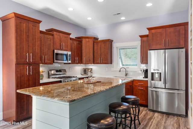 kitchen featuring light hardwood / wood-style floors, stainless steel appliances, sink, a breakfast bar, and a center island