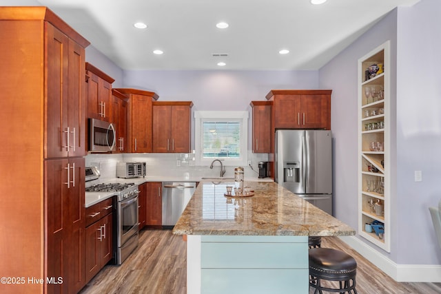 kitchen with light hardwood / wood-style floors, a kitchen bar, stainless steel appliances, light stone counters, and a center island