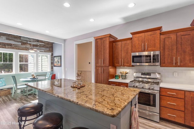 kitchen with tasteful backsplash, light hardwood / wood-style floors, a kitchen breakfast bar, stainless steel appliances, and light stone counters