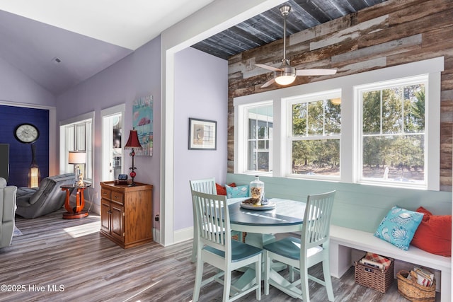 dining room with wood walls, ceiling fan, lofted ceiling, and wood-type flooring