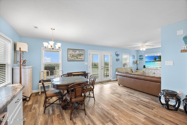 dining space with a wealth of natural light, french doors, wood-type flooring, and ceiling fan with notable chandelier