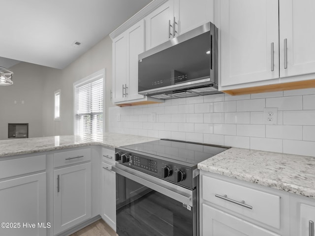 kitchen with light stone counters, white cabinets, decorative backsplash, range with electric stovetop, and stainless steel microwave