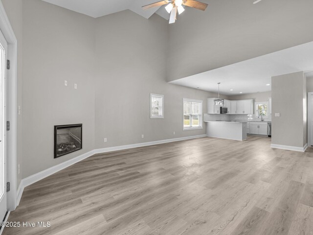 unfurnished living room with ceiling fan, baseboards, a glass covered fireplace, and light wood-type flooring