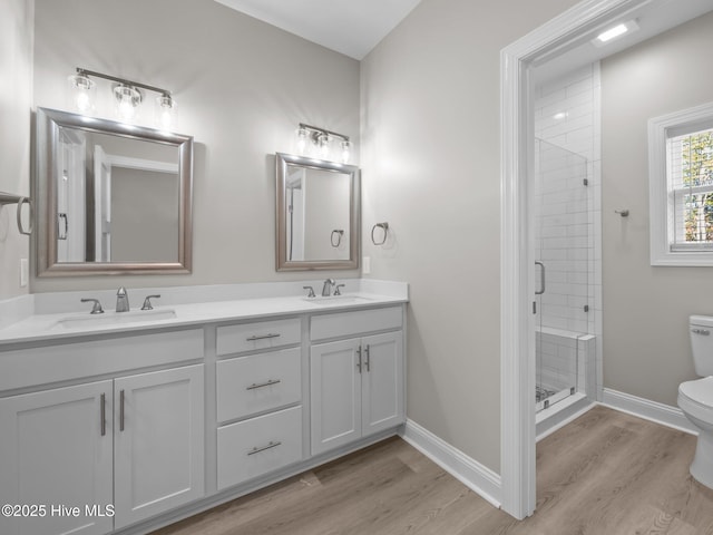 bathroom featuring a shower stall, wood finished floors, toilet, a sink, and baseboards