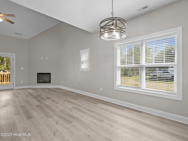 unfurnished living room featuring vaulted ceiling, visible vents, light wood-style floors, and a healthy amount of sunlight