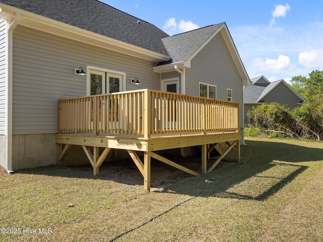 rear view of house featuring a wooden deck, a lawn, and roof with shingles