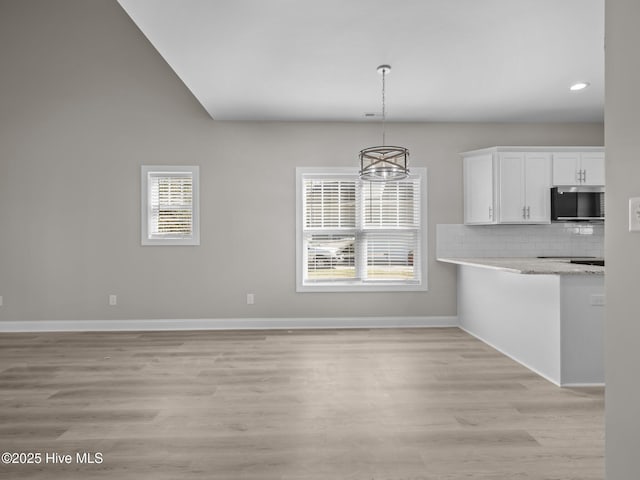 kitchen with stainless steel microwave, light wood-style floors, baseboards, hanging light fixtures, and white cabinetry