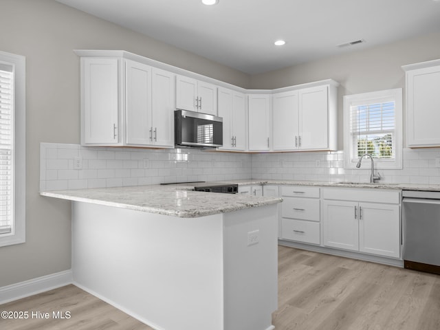 kitchen featuring stainless steel appliances, a sink, light wood-type flooring, a peninsula, and white cabinetry