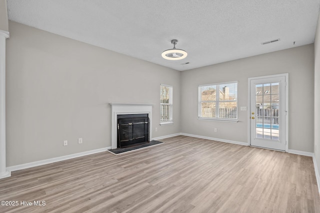2214 Splitbrook Ct, Wilmington, NC 28411 - unfurnished living room with light wood-style floors, healthy amount of natural light, a textured ceiling, baseboards, and a glass covered fireplace