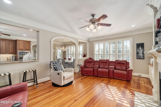 living room with a premium fireplace, ornamental molding, ceiling fan with notable chandelier, and light wood-type flooring