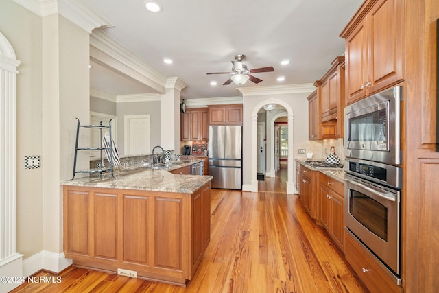 kitchen featuring light stone counters, appliances with stainless steel finishes, kitchen peninsula, light hardwood / wood-style floors, and backsplash