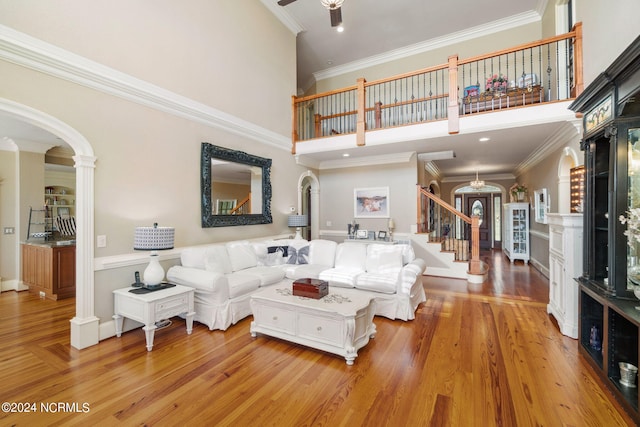 living room with crown molding, a towering ceiling, ceiling fan, and light wood-type flooring