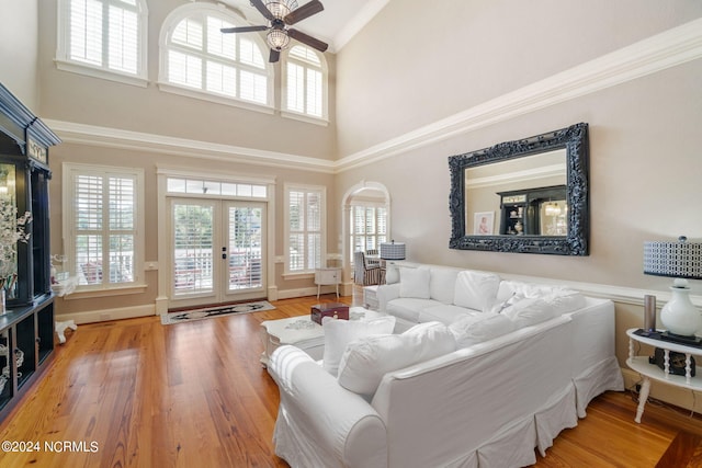 living room featuring a towering ceiling, hardwood / wood-style flooring, ornamental molding, ceiling fan, and french doors