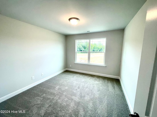 empty room featuring visible vents, dark carpet, and baseboards