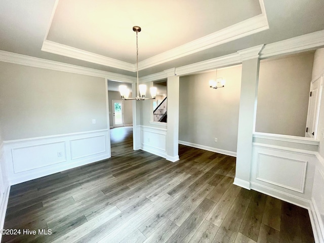 unfurnished dining area with crown molding, a raised ceiling, dark wood-type flooring, a chandelier, and stairs