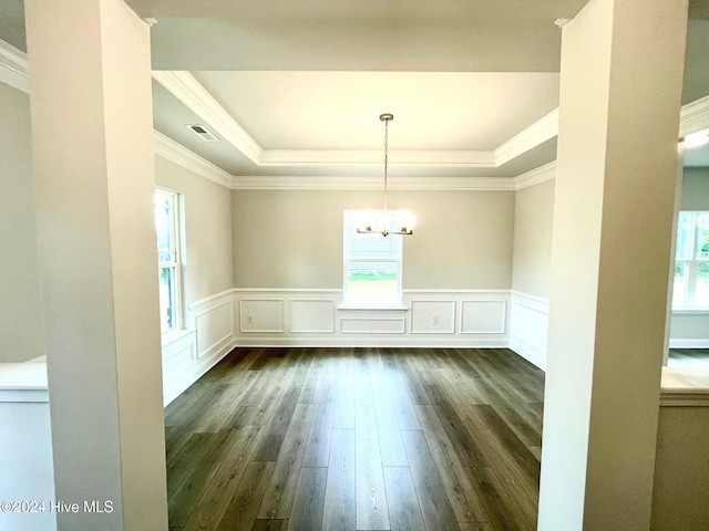 unfurnished dining area with dark wood-type flooring, a tray ceiling, a wainscoted wall, and an inviting chandelier