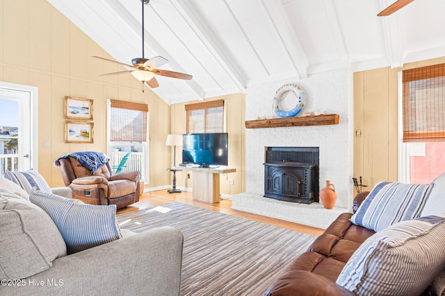 living room with light wood-type flooring, ceiling fan, a wood stove, and vaulted ceiling with beams