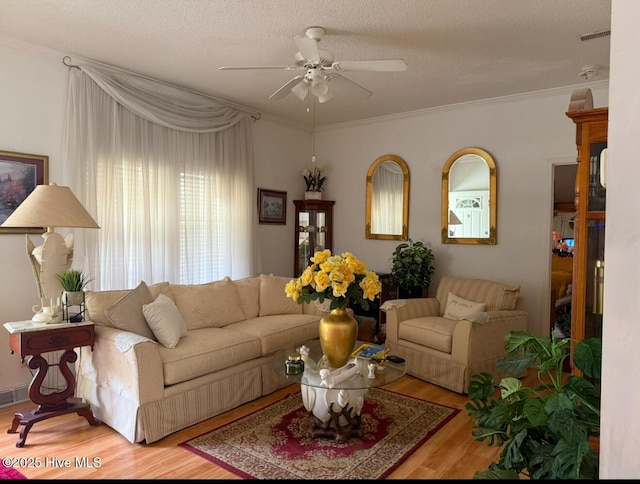 living area with wood finished floors, visible vents, crown molding, a textured ceiling, and ceiling fan