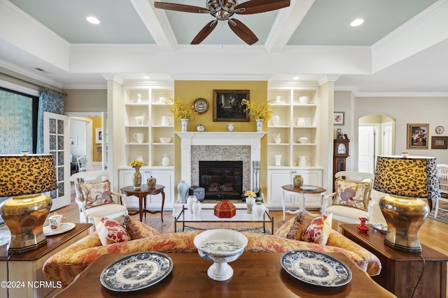 living room with beamed ceiling, built in shelves, crown molding, and a tiled fireplace