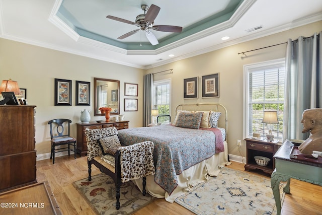 bedroom with ceiling fan, light hardwood / wood-style floors, a raised ceiling, and crown molding