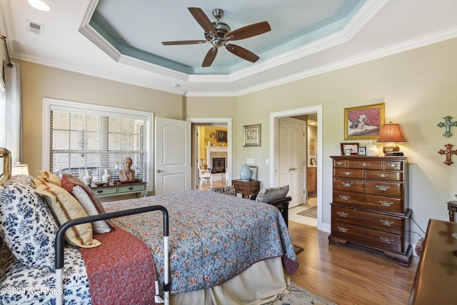 bedroom with hardwood / wood-style floors, ceiling fan, a raised ceiling, and ornamental molding